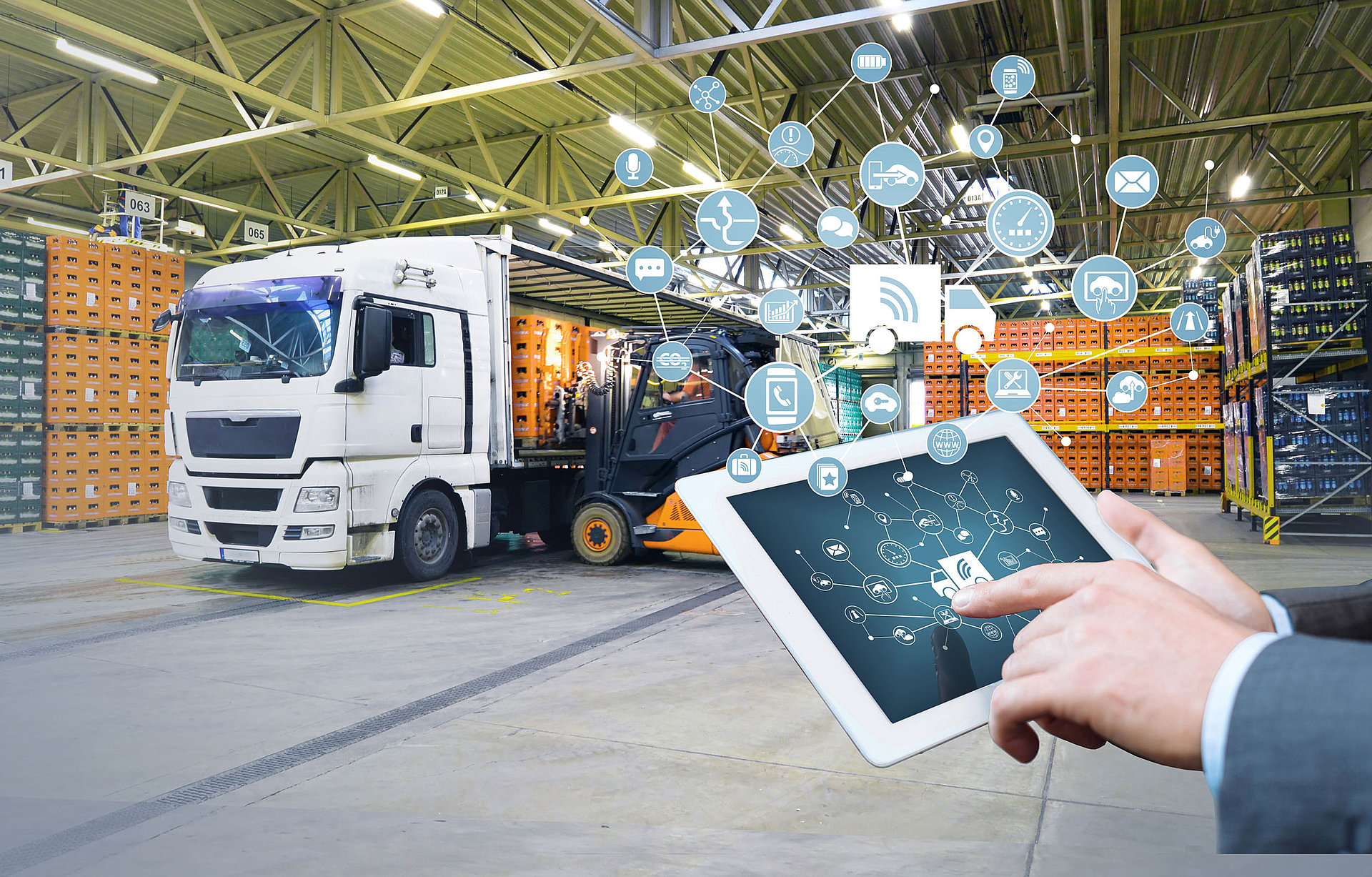Finger zeigt auf ein Tablet mit vernetzten Symbolen und im Hintergrund wird ein LKW mit Kisten beladen